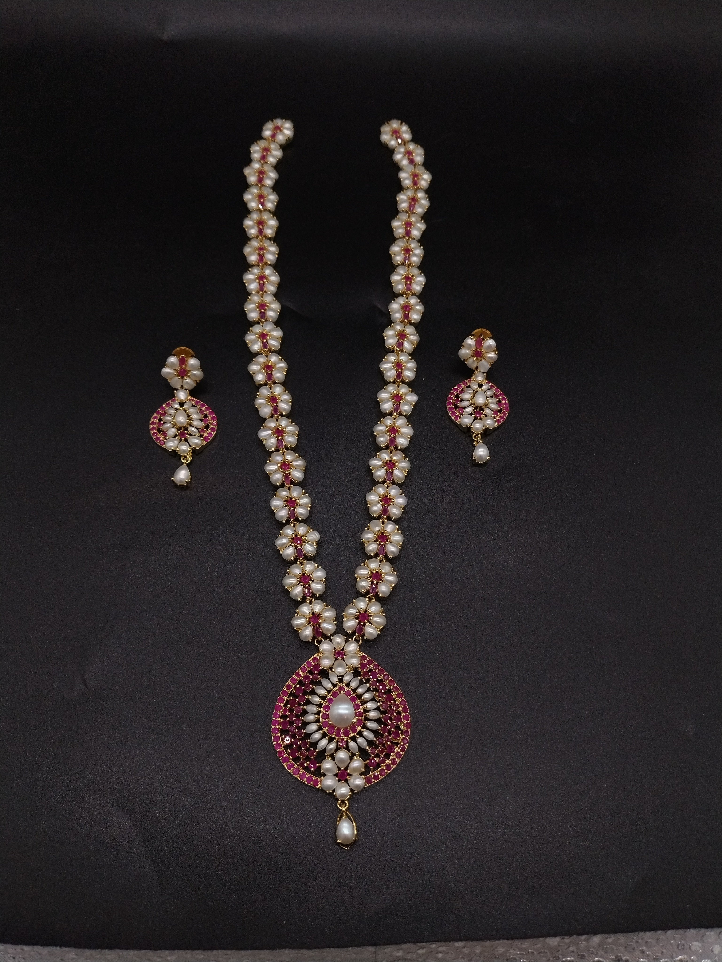 Freshwater pearl long haram set with floral pearl clusters, red stone accents, circular centerpiece, and matching earrings.