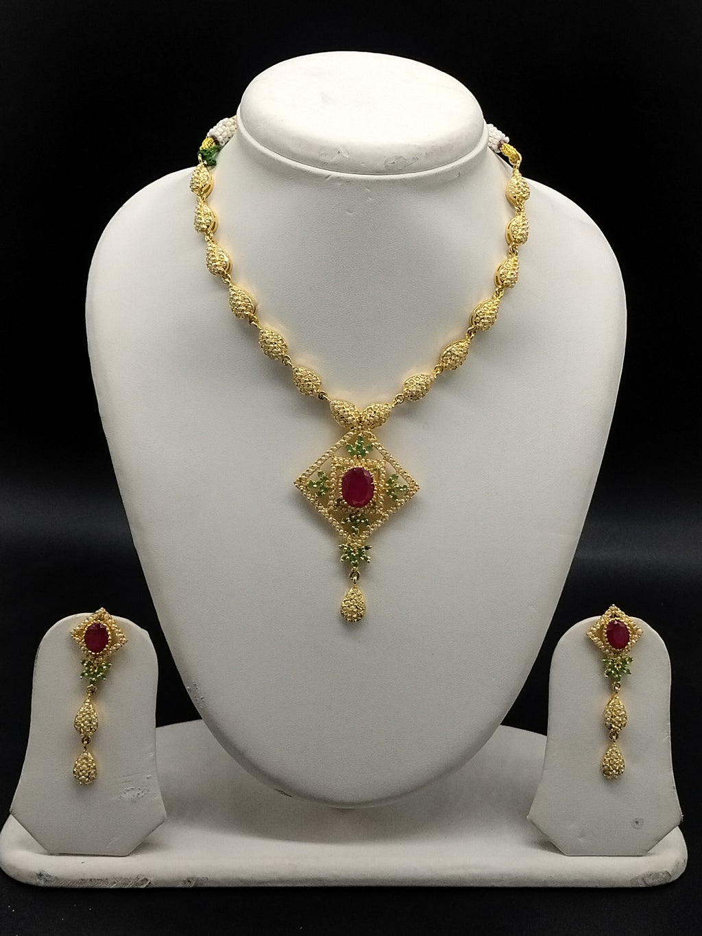 Freshwater pearl necklace set with ruby red and emerald green stones, diamond-shaped pendant, and matching hanging earrings.