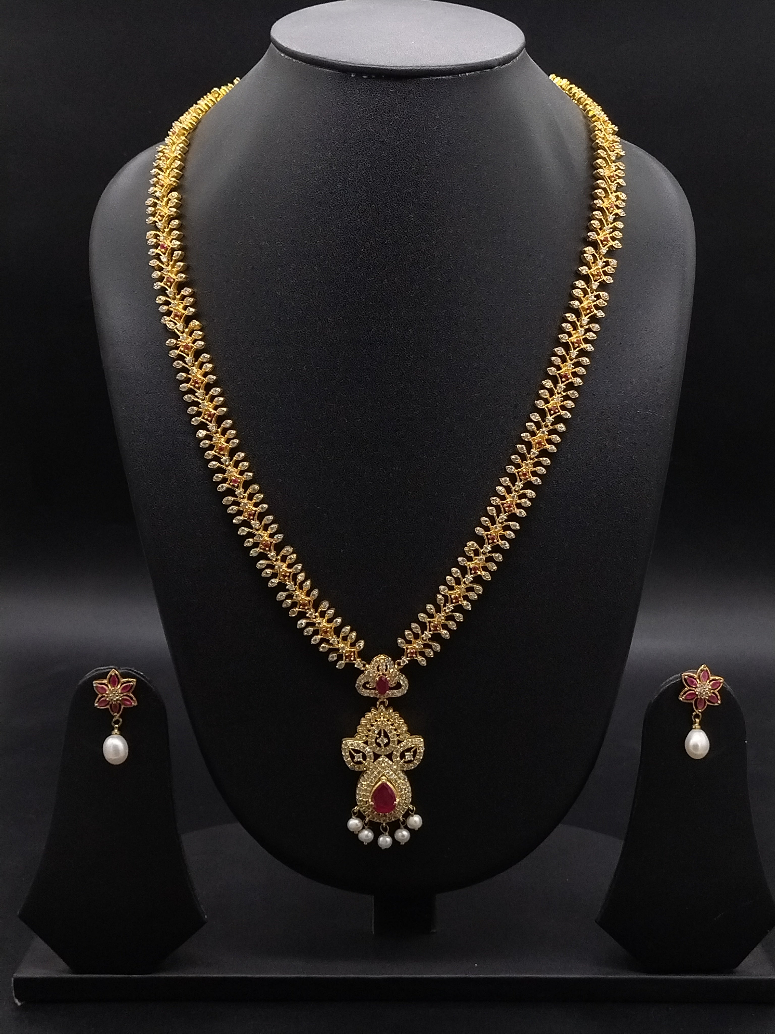 Long haram set with red and white American Diamond stones, ornate floral pendant, pearl drops, and matching earrings.