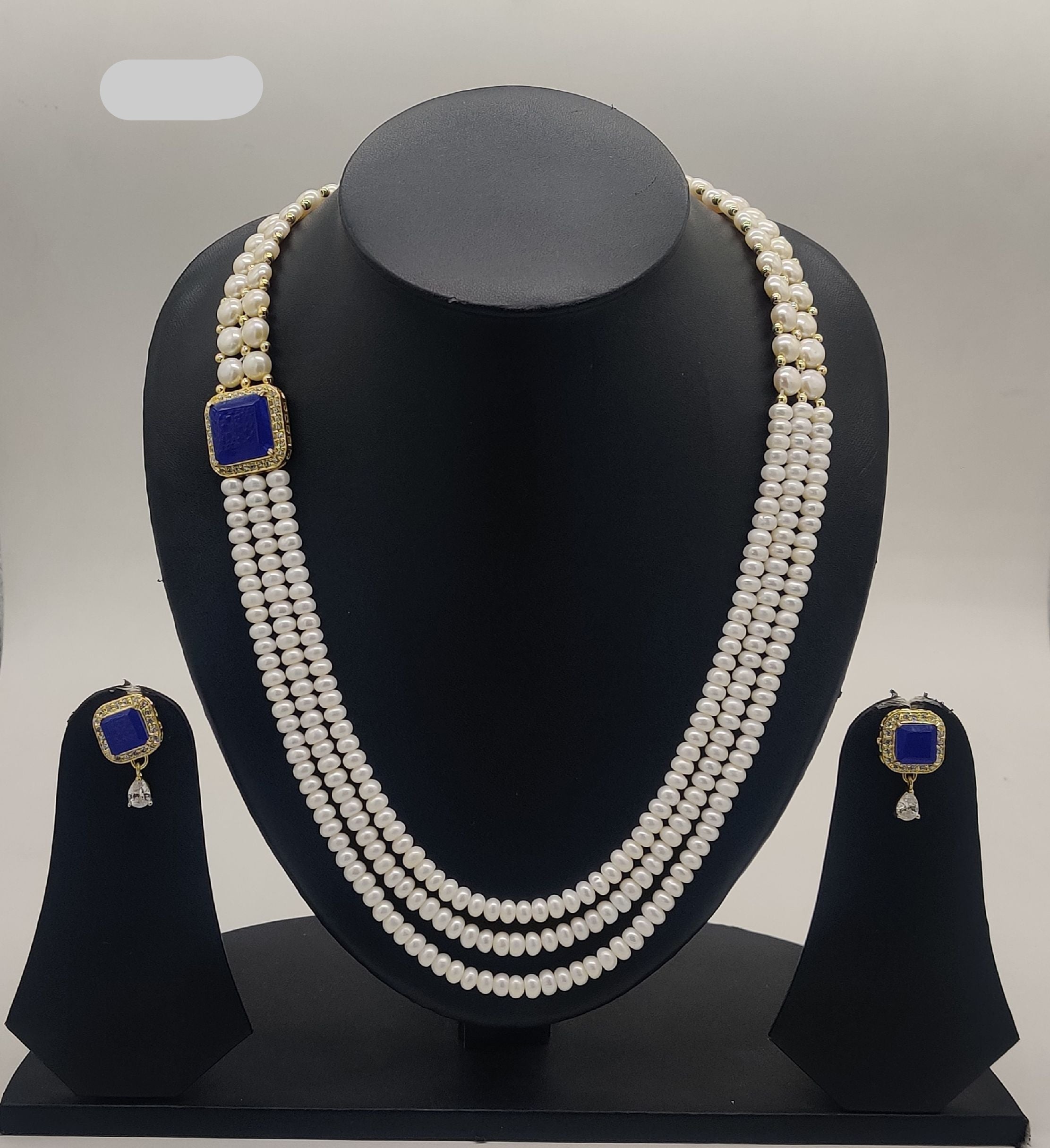 Multi-line freshwater pearl broach set with square sapphire-blue stone centerpiece and matching stud earrings.