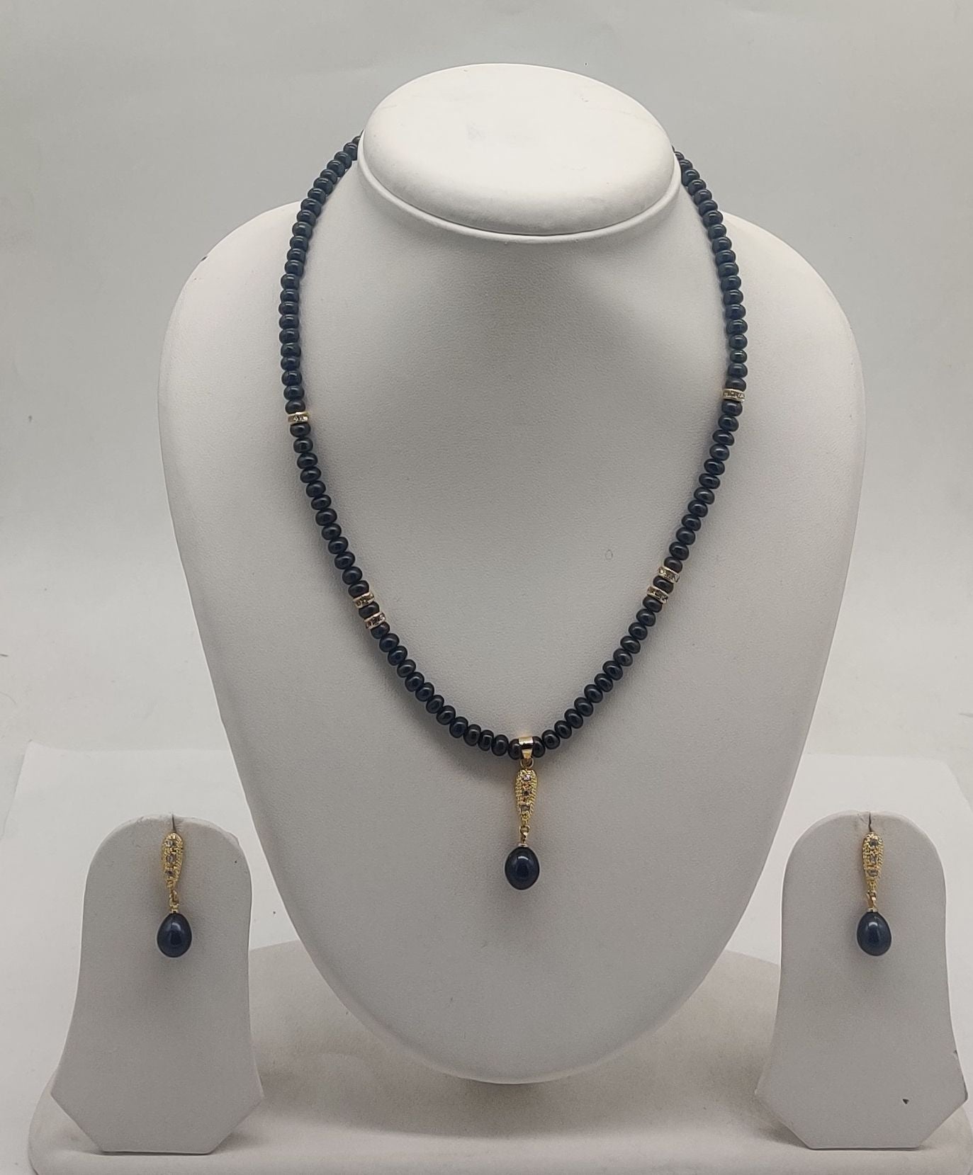 One line freshwater pearl necklace and earrings set with dark beads, gold accents, and black teardrop pendant